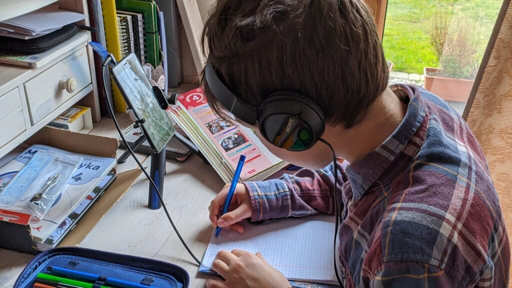 Young boy writing notes during an online class at home, focused on studying.